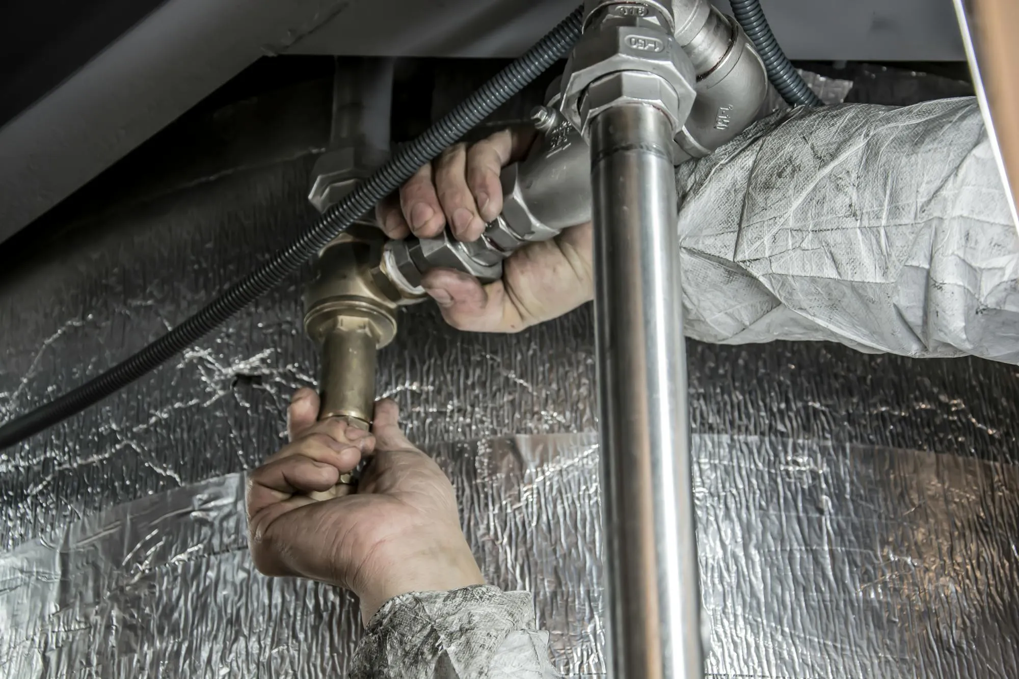 Plumber's hands tightening a copper pipe in a Liverpool kitchen, dim morning light